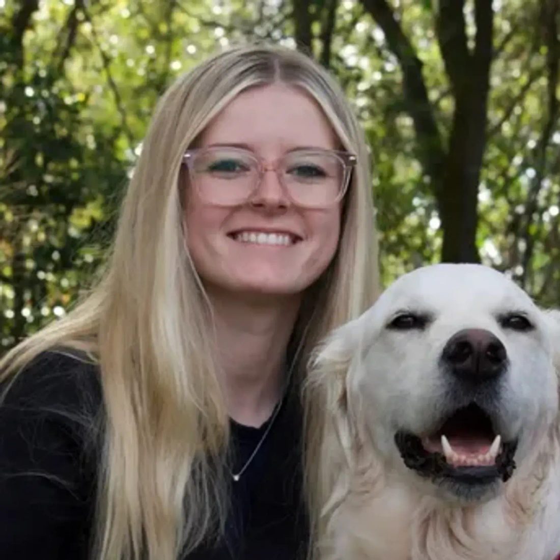 Blonde woman with glasses posing with a golden retriever outdoors