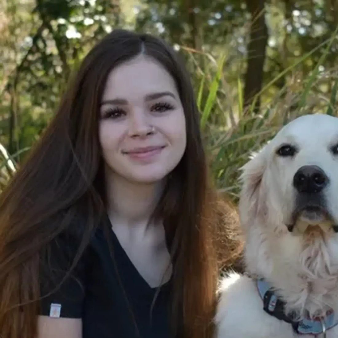 Brunette woman smiling with a golden retriever in a grassy area