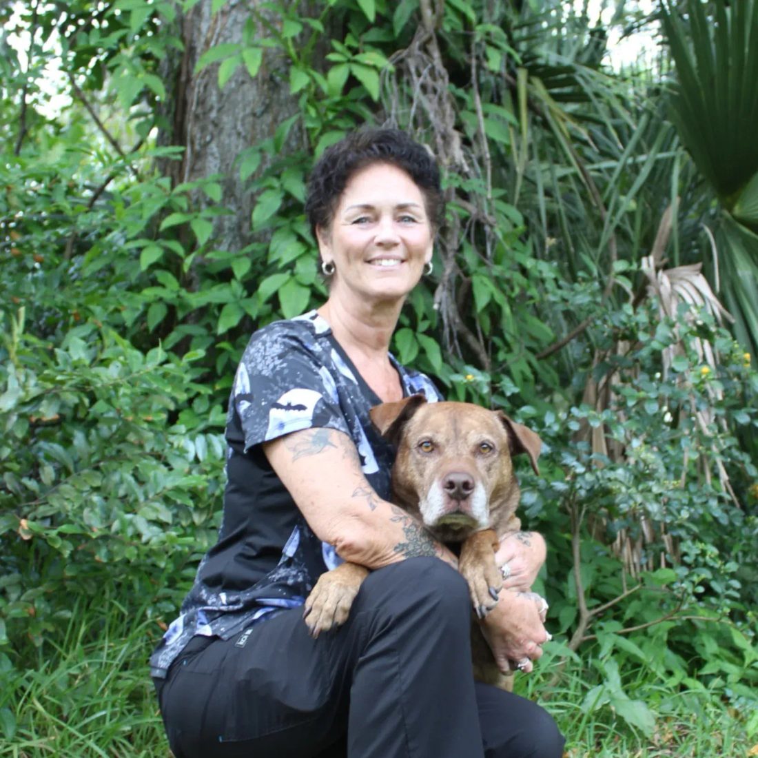 Woman crouching with a brown dog in a lush garden setting