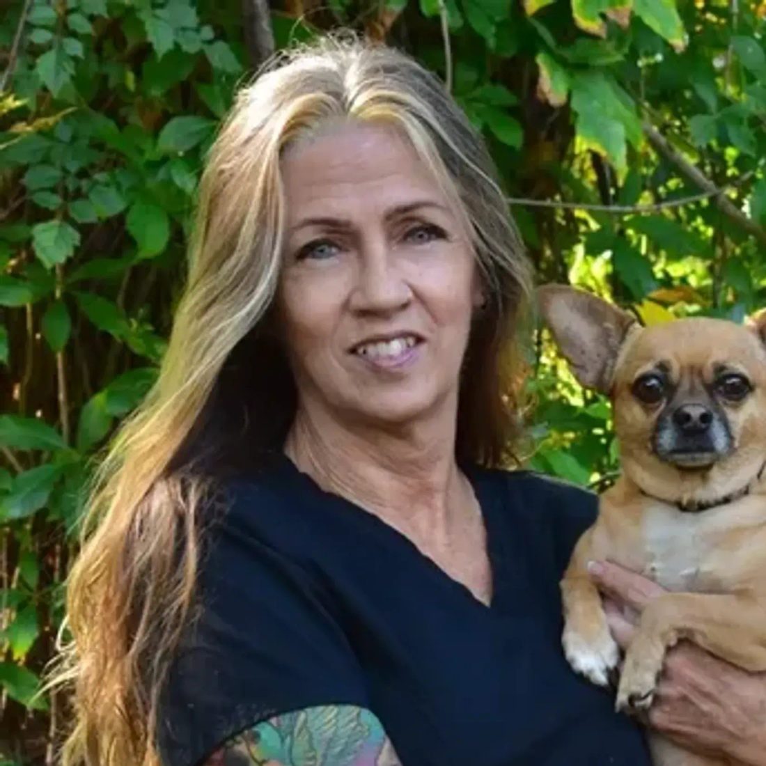 Woman with tattooed arm holding a small chihuahua outdoors